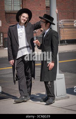 2 orthodoxe jüdische Jungen mit langem gelocktem Peyus unterhalten sich an einem milden Spätsommertag freundlich und lebhaft. Stockfoto