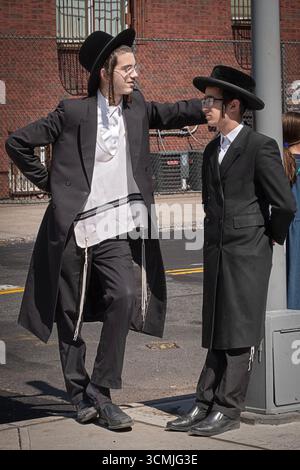 2 orthodoxe jüdische Jungen mit langem gelocktem Peyus unterhalten sich an einem milden Spätsommertag freundlich und lebhaft. Stockfoto