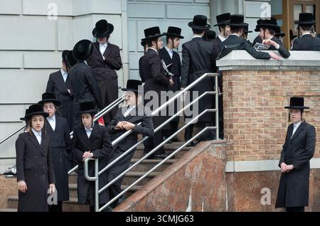 Ähnlich gekleidete Yeshiva-Schüler treffen sich zusammen und warten auf einen Bus, um dann zu einer saisonalen Gebetssitzung zu fahren. In New York City. Stockfoto