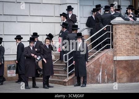Ähnlich gekleidete Yeshiva-Schüler treffen sich zusammen und warten auf einen Bus, um dann zu einer saisonalen Gebetssitzung zu fahren. In New York City. Stockfoto