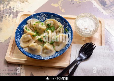 Ein Teller mit russischen Knödeln mit Sauerrahm und frischem Dill auf einem Holzbrett, serviert auf Bastelpapier. Stockfoto