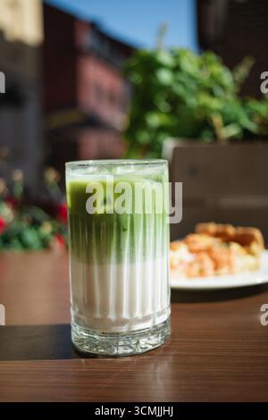 Nahaufnahme eines gefrorenen Matcha Latte und ein Stück Lachsquiche auf einem Café-Tisch im Freien im Sommer Stockfoto