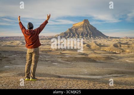 Rückansicht eines Mannes, der mit den Armen in der Luft vor Factory Butte in den Upper Blue Hills, Wayne County, Utah, USA steht Stockfoto