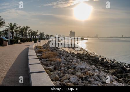 Blick auf die Promenade mit Palmen und felsiger Küste entlang des Arabischen Golfs bei Sonnenuntergang in Kuwait City, Kuwait. Kuwait Stadt, Kuwai Stockfoto