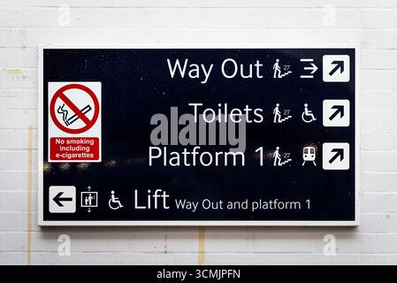 Wegweiser im britischen Bahnhof, die den Ausweg zeigen, Toiletten, Bahnsteig 1, Zugang zum Aufzug und Rauchverbot. Stockfoto