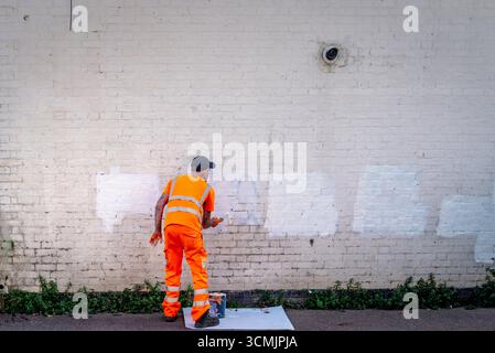Gemeindearbeiter in High-Visibility-Kleidung, die über Graffiti auf einer Ziegelwand malt Stockfoto