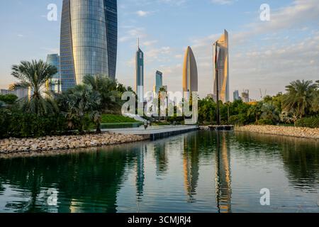 Malerischer Blick auf den Al Shaheed Park in Kuwait City, mit üppigem Grün, einem reflektierenden Wasserspiel und modernen Wolkenkratzern, einschließlich Al Hamra Tower, Stockfoto