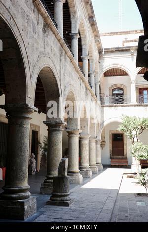 Steinbögen und Säulen säumen einen sonnendurchfluteten Innenhof im Instituto Cultural Cabañas in Guadalajara Stockfoto