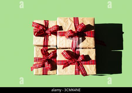 Vier Geschenkboxen in braunem Papier mit rotem kariertem Band auf grünem Hintergrund für die Weihnachtsfeiertage. Stockfoto