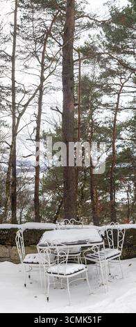 Eine ruhige Szene im Freien mit schneebedecktem Metalltisch und Stühlen in der Winterlandschaft Stockfoto