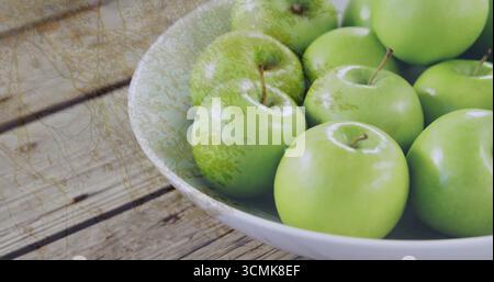 Weiße Keramikschale mit glänzenden grünen Äpfeln auf hölzernem Küchentisch, Kopierraum Stockfoto