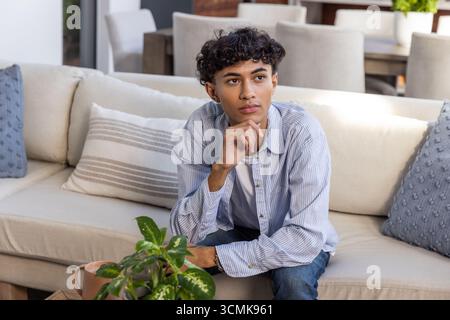 Mann, der zu Hause auf dem Sofa sitzt, trägt Hemd, der sich an der Hand am Kaffeetisch beugt, Pflanze Stockfoto