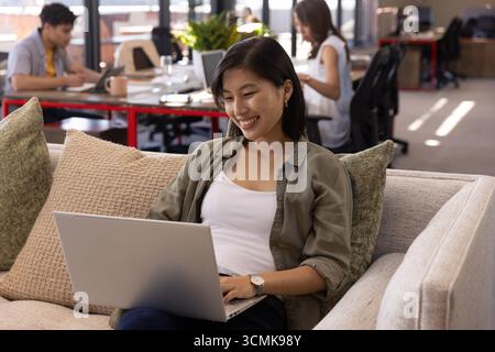 Verschiedene Kollegen arbeiten in der Bürolounge mit silbernem Laptop, Tablet, Kaffeetasse, Topfpflanze Stockfoto
