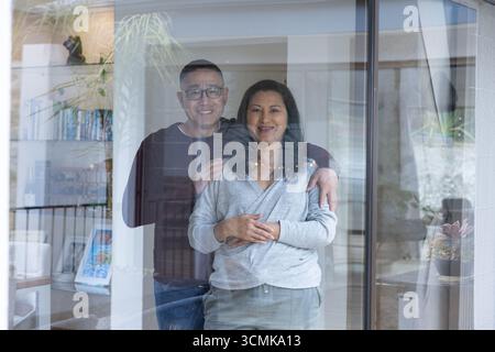 Senior chinese Mann und Frau stehen hinter Schiebetür im Wohnzimmer neben dem Bücherregal Stockfoto