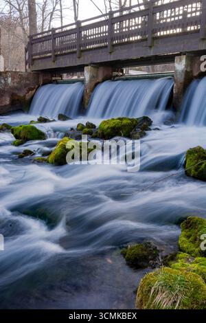 Eine Fußgängerbrücke, die über einen kleinen Wasserfall in einem Forellenpark in Missouri führt. Stockfoto