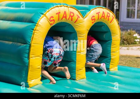 Zwei Kinder krabbeln auf einer Geburtstagsparty durch aufblasbares Spiel und haben Spaß an einem sonnigen Sommertag Stockfoto