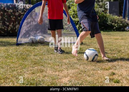 Zwei Kinder spielen Fußball im Garten an einem sonnigen Sommertag und treten den Ball auf ein kleines Tor Stockfoto
