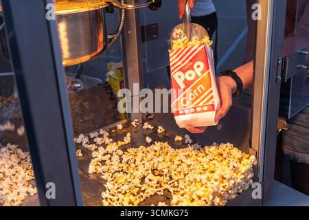 Straßenverkäufer schöpfen frisches, heißes Popcorn aus einer Maschine in eine Papiertüte und servieren bei einer lebhaften Veranstaltung im Freien einen köstlichen Snack Stockfoto