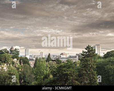 Erhöhtes Panorama in Richtung Paris vom Parc des Buttes Chaumont, mit einer breiten Skyline mit Türmen und Dächern über Bäumen unter bewölktem Himmel, Förderanlagen Stockfoto