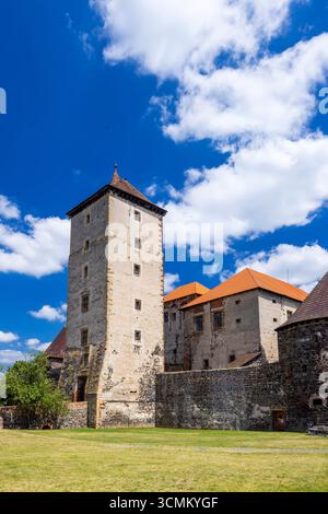Mittelalterliche Svihov Wasserburg mit einem hohen Turm und einem orangen Dach, das unter blauem Himmel mit weißen Wolken in Svihov, Tschechien, aufsteigt Stockfoto