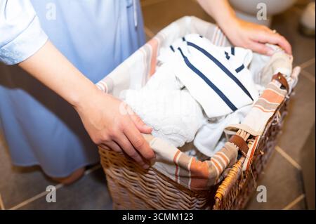 Weibliche Hände, die einen Wäschekorb mit schmutziger Kleidung halten, Konzept der Hausarbeit und Haushaltsroutine Stockfoto