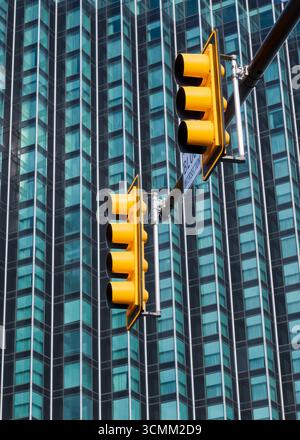 Gelbe Ampelkreuzung auf der Säule gegen Glasgebäude. Stockfoto