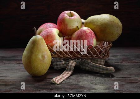 Reife rote Äpfel in einem Korb mit reifer Birne auf einem Holztisch Stockfoto