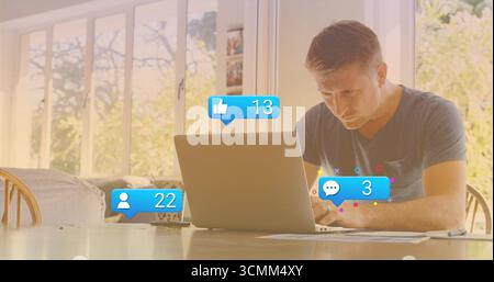 Reifer Mann, der auf silbernem Laptop im Essbereich tippt, mit Papierkolben und sozialen Ikonen Stockfoto