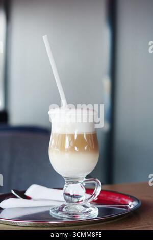 Ein geschichteter Latte mit schaumiger Milch, serviert in einem klaren Glas auf einem silbernen Tablett mit Strohhalm Stockfoto