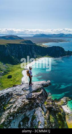 Erkunden Sie die atemberaubende Aussicht vom Matind Mountain in Bleik, Andoya, wo zerklüftete Klippen auf das glitzernde türkisfarbene Wasser treffen. Ein Wanderer steht selbstbewusst am Rande und genießt die Schönheit der Natur. Stockfoto