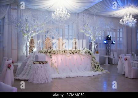 Ein wunderschön gestalteter Hochzeitsempfang verfügt über einen großen Kopftisch mit üppigen Blumenarrangements und weichen weißen Stoffen. Stockfoto