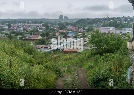 Panoramablick auf Hochleitungen und Wohndächer in Korsakow, Russlands Sachalin-Region, mit Baukränen auf einem grünen Hang. Stockfoto