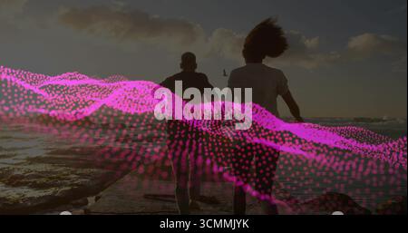 Ein Laufpaar trägt T-Shirts und Shorts, die sich bei Sonnenuntergang der Küste nähern, mit rosafarbenem Wellenüberzug Stockfoto