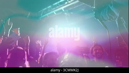 Konzertbesucher heben die Hände und nehmen in intimer Atmosphäre mit farbigem Licht auf Smartphones auf Stockfoto