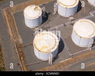 Die Luftaufnahme erfasst vier weiße industrielle Brennstofftanks mit Rostspuren. Die Szene vermittelt eine industrielle, utilitaristische Stimmung in einer leeren Außenseite Stockfoto