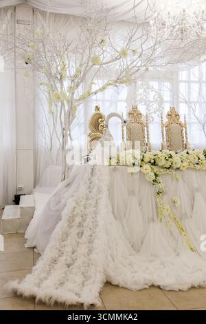 Ein wunderschön gestalteter Hochzeitstisch für Braut und Bräutigam bietet lebendige Pfauenfedern und zarte Perlen. Blumendekoration und elegantes Dekor Stockfoto