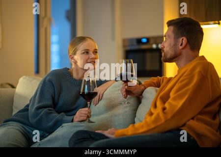 Romantischer Abend mit Wein unter schlechten Lichtverhältnissen, das Paar unterhält sich im intimen Wohnzimmer. Paare sprechen Stockfoto