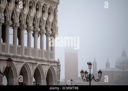 Nebel umhüllt die Bögen des Dogenpalastes in Venedig, während der campanile von San Giorgio Maggiore in den Winternebel eintaucht und eine ruhige Szene schafft. Stockfoto