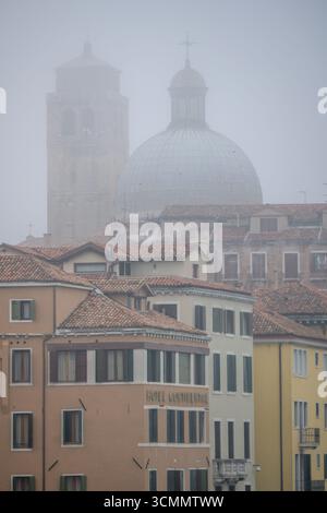 Der Glockenturm und die Kuppel von San Geremia erscheinen im Winternebel sanft und verschmelzen mit Cannaregios Architektur in einer ruhigen venezianischen Szene. Stockfoto