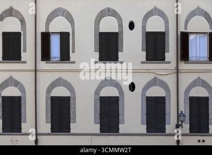 338 Reihen spitzer Steinbögen über rechteckigen Fenstern an der verputzten, cremefarbenen Wand eines Gebäudes auf der Piazza Mentana. Florenz-Toskana Stockfoto