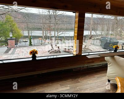 Jenkintown, Pennsylvania, USA - 01. April 2025: Gemütliche Holzeinrichtung mit Blick auf einen bezaubernden See und eine Terrasse mit Sonnenblumen. Stockfoto