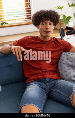 afroamerikaner, der in ein Popfilter-Mikrofon spricht, auf dem Sofa im Wohnzimmer Gesten macht Stockfoto
