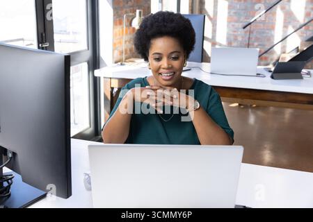 afroamerikanerin, die an einem silbernen Laptop arbeitet, am modernen Loft-Schreibtisch mit Monitor Stockfoto