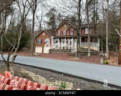 Jenkintown, Pennsylvania, USA - 01. April 2025: Rustikales Holzhaus umgeben von Bäumen, komplett mit Veranda und Auffahrt Stockfoto