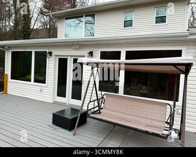 Jenkintown, Pennsylvania, USA - 01. April 2025: Wohnterrasse mit beigefarbenem Schaukelsitz und großen Fenstern Stockfoto