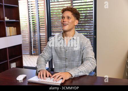 Mann, der mit der Maus auf einer weißen Tastatur am Holzschreibtisch mit Bücherregal und Schiebetüren tippt Stockfoto