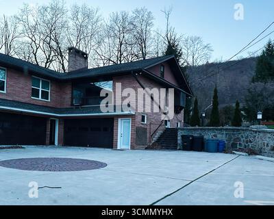 Jenkintown, Pennsylvania, USA - 01. April 2025: Ein geräumiges Backsteinwohnhaus mit Auffahrt, umgeben von einem ruhigen Wald. Stockfoto