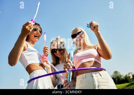 Fröhliche Freunde feiern draußen mit Blasen und Lachen unter einem sonnigen Himmel Stockfoto