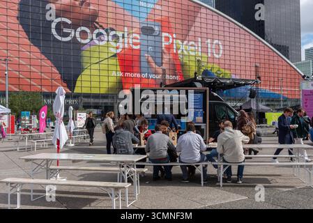 Leute essen Burger auf einer Terrasse im Geschäftsviertel La Défense, Paris. Leute, die in der Warteschlange stehen, um Burger von einem Imbisswagen zu kaufen Stockfoto