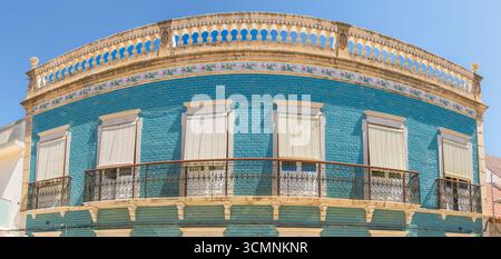 Geschwungene Fassade eines alten Gebäudes, das mit blauen Fliesen bedeckt ist, mit geschlossenen Fensterläden, Blumendekorationen und schmiedeeisernen Balkonen. Stockfoto